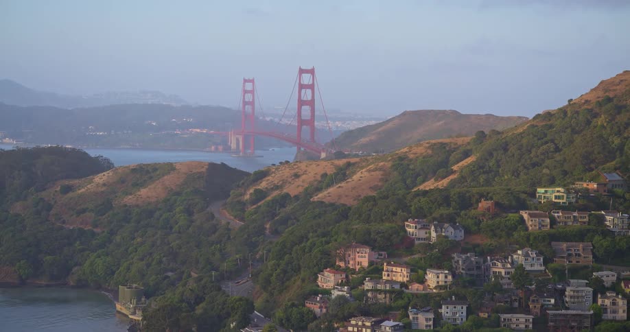 A slow zoom out reveals the beautiful hillside homes of Sausalito with the iconic Golden Gate Bridge in the background on a hazy morning