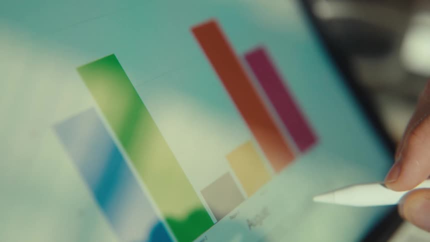 A business professional analyzes a colorful bar chart of monthly data on a tablet using a digital pen