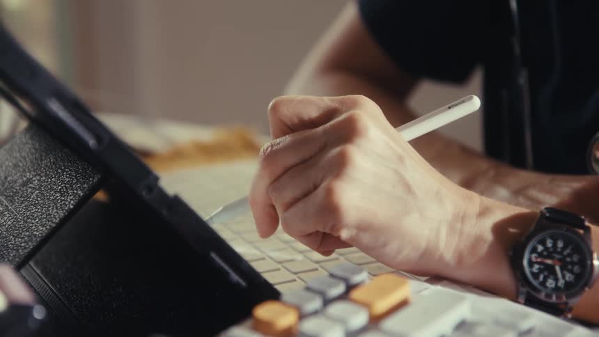 A close-up view shows a doctor's hand using a digital stylus to take notes or design on a tablet at their desk