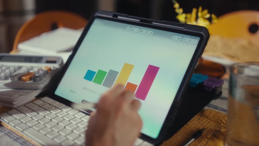 An analyst reviews and modifies a colorful bar chart on a tablet screen using a stylus while working at a desk
