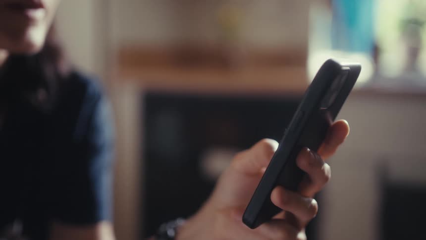 Cinematic slow-motion close-up of a hand holding and scrolling on a black smartphone indoors