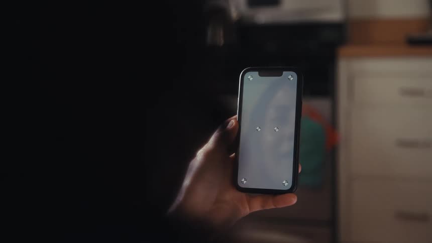 Over the shoulder shot of a woman holding a smartphone with a screen ready for replacement in her sunlit kitchen