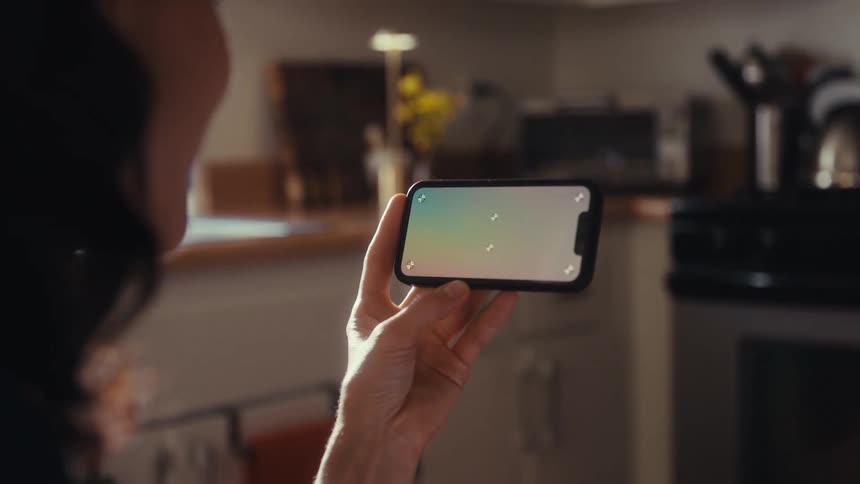 Over the shoulder view of a woman holding a smartphone horizontally with a screen ready for custom content in a bright kitchen