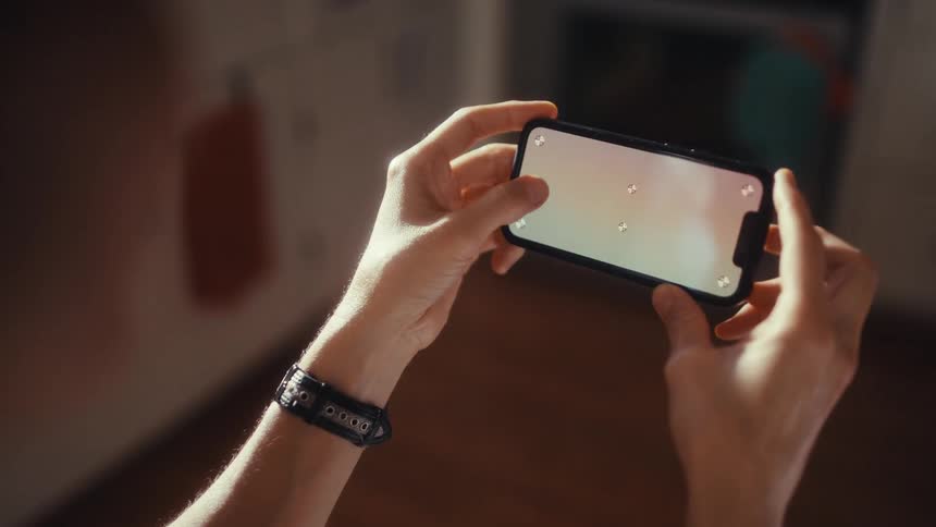 Over-the-shoulder view of hands holding a smartphone horizontally with a green screen display and tracking markers