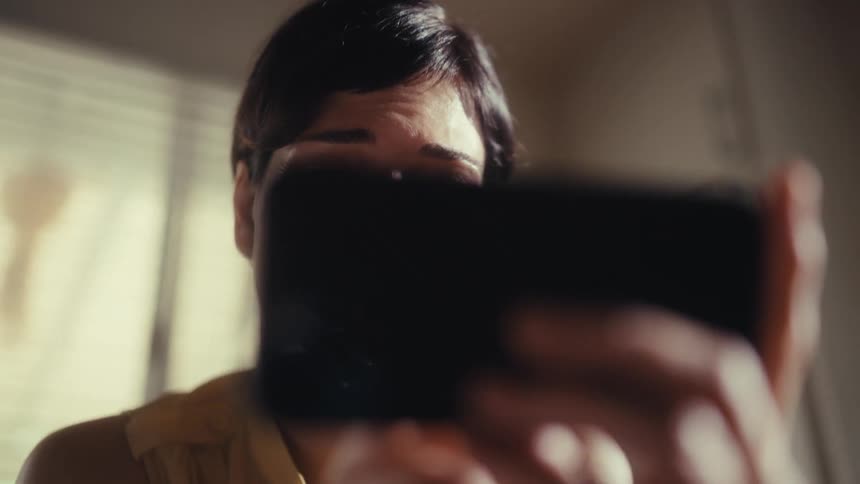 A joyful woman smiles as she watches content on her smartphone in slow motion