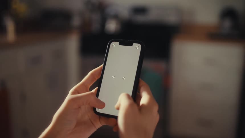 Close-up over-the-shoulder view of a person using a smartphone with a blank screen featuring tracking markers, slowly zooming out