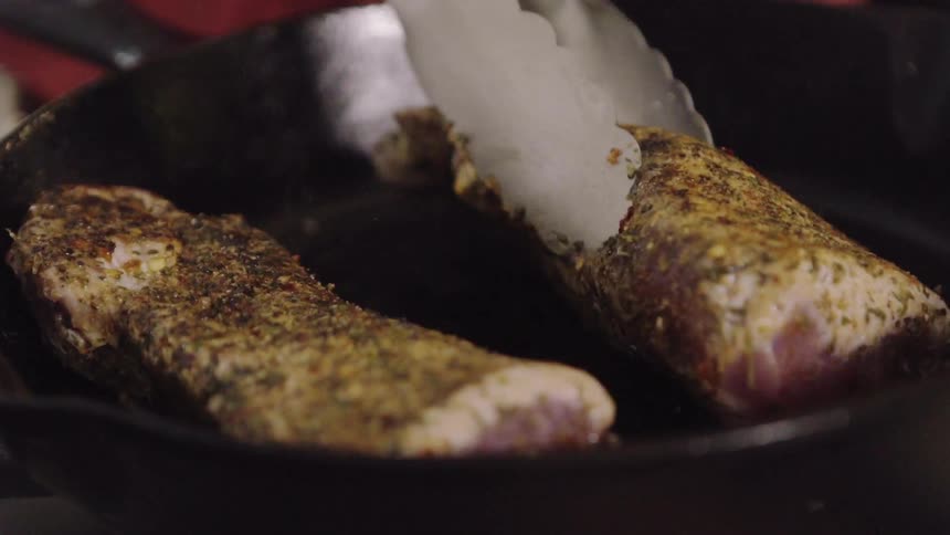 A person flips some cooking meat in a pan