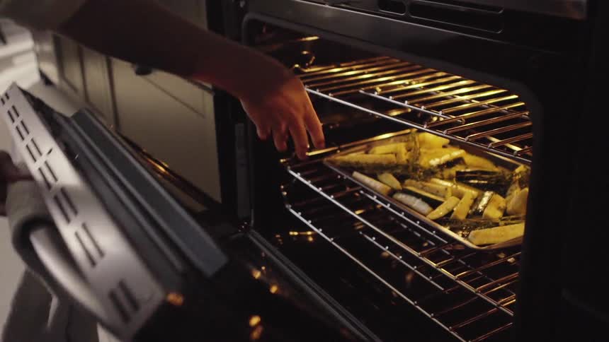 A person puts a plate of vegetables in the oven