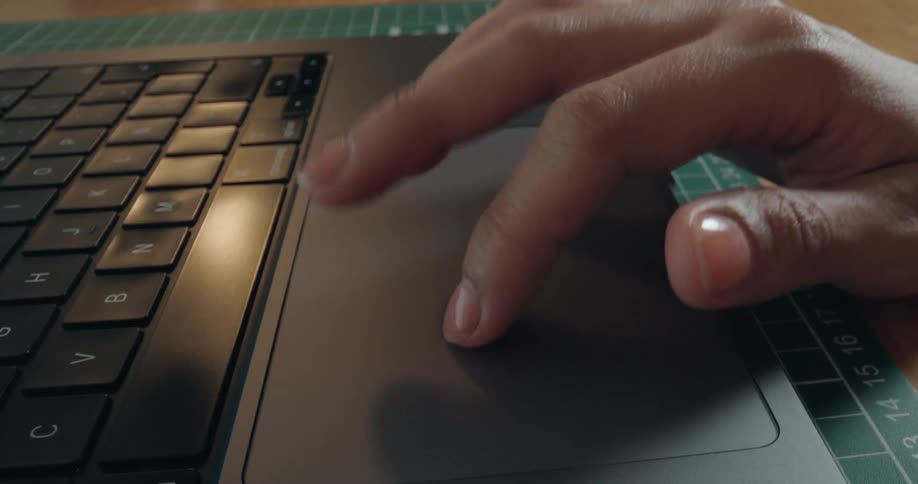 A detailed close-up of a person's fingers scrolling and navigating on the trackpad of a sleek, modern laptop