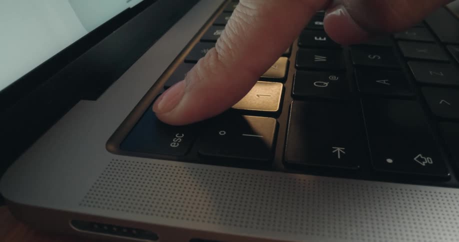 A dynamic close-up shot focuses on a finger pressing the 'esc' key on a laptop keyboard