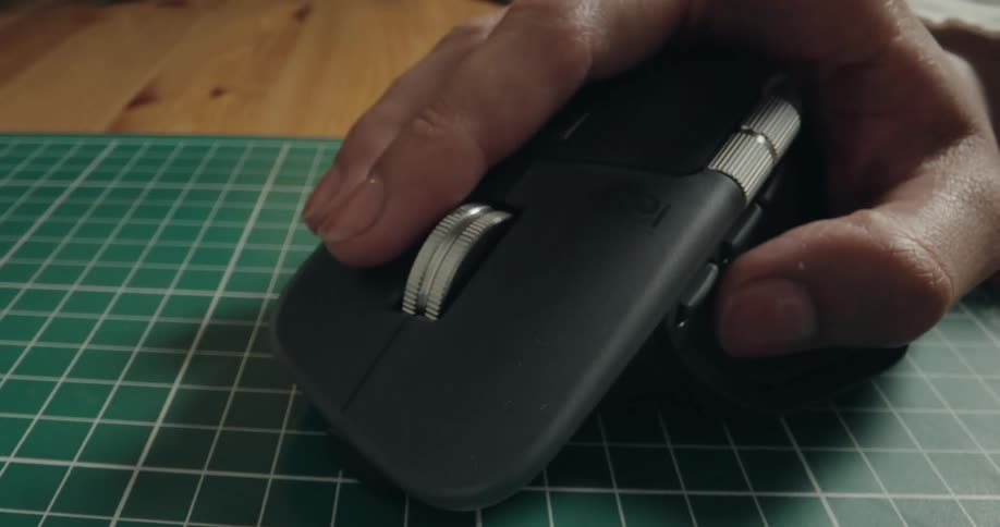 A close-up shot of a person's hand using a computer mouse, scrolling with the middle finger on a green gridded mouse pad