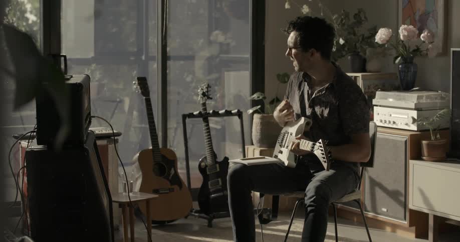 A man is playing a guitar and taking composition notes