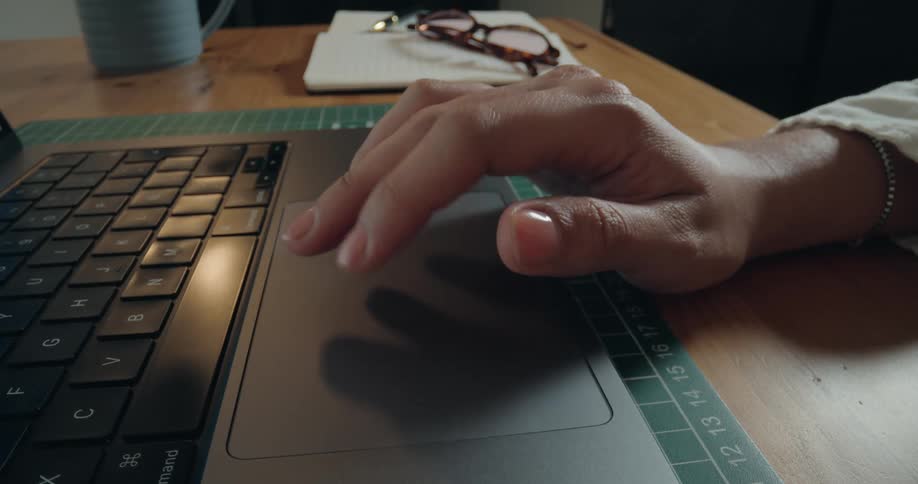Close-up cinemagraph of a hand scrolling and clicking on a laptop trackpad on a desk