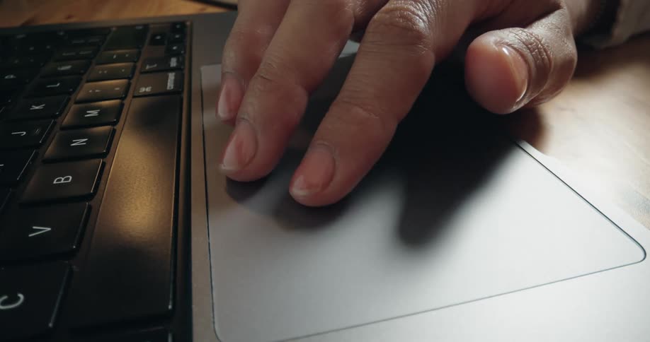 A detailed close-up shot of a person's hand using the trackpad on a modern laptop computer