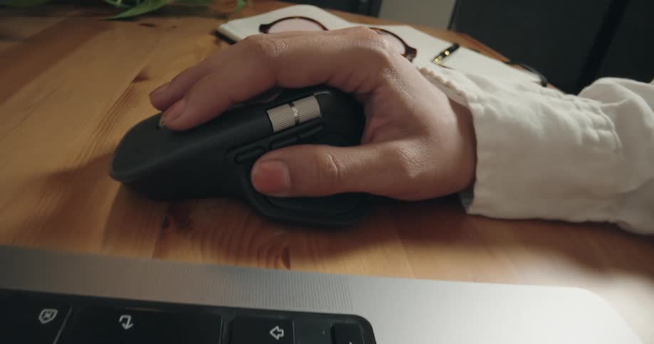 Dynamic close-up shot of a person working on a laptop, focusing on their hand using a wireless ergonomic mouse