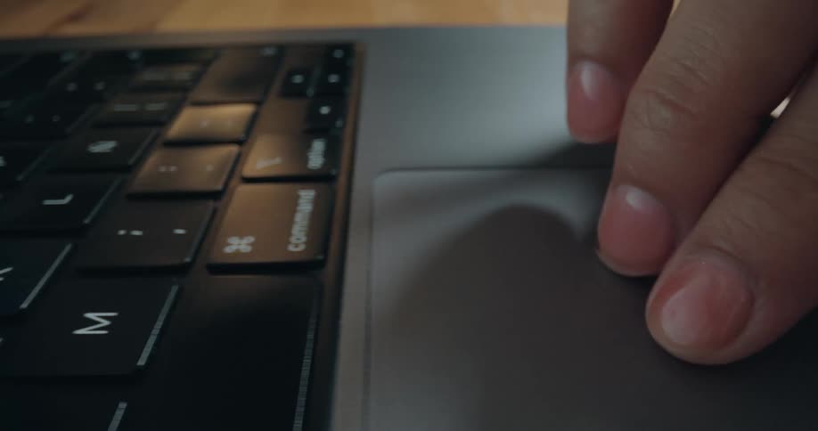 A close-up of a person's fingers using the trackpad on a sleek laptop keyboard