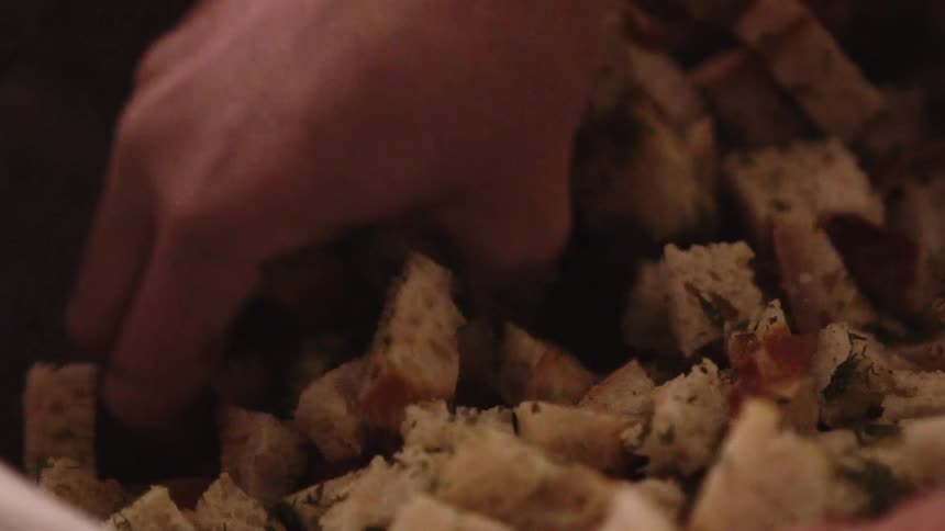 A woman is mixing croutons with herbs in a bowl with her hand