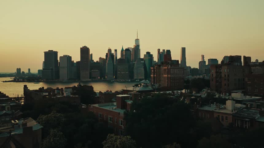 A slow aerial pullback reveals the Brooklyn rooftops with the Manhattan skyline glowing at sunset