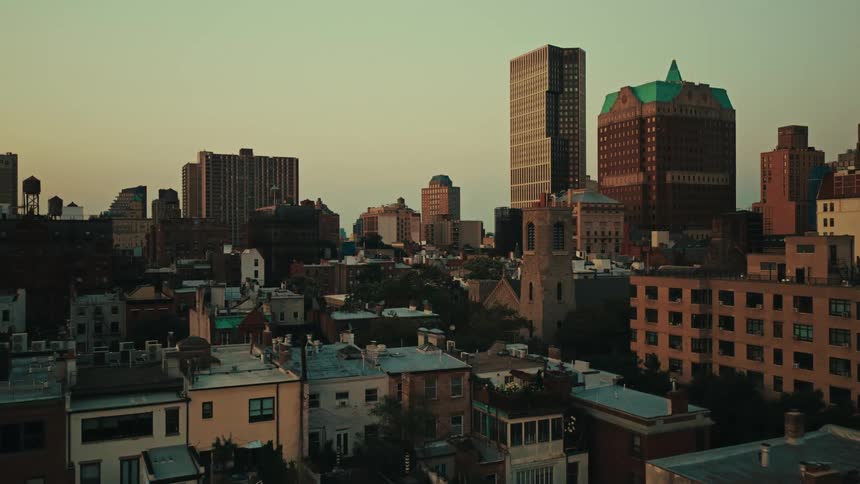An aerial view slowly pushes in over the rooftops of Brooklyn Heights at sunset, revealing a historic church nestled among modern skyscrapers