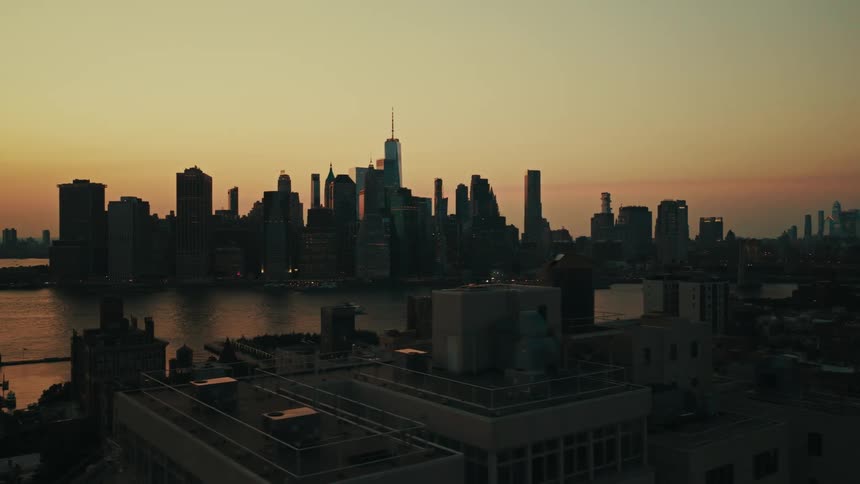 Slowly pulling back over Brooklyn rooftops to reveal the magnificent New York City skyline and the East River during a breathtaking sunset