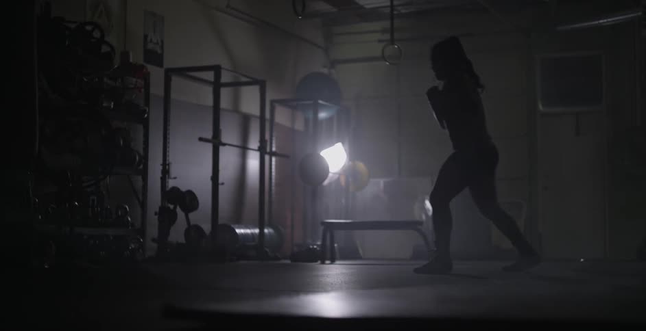 Woman punches and jumps in a dimly lit gym