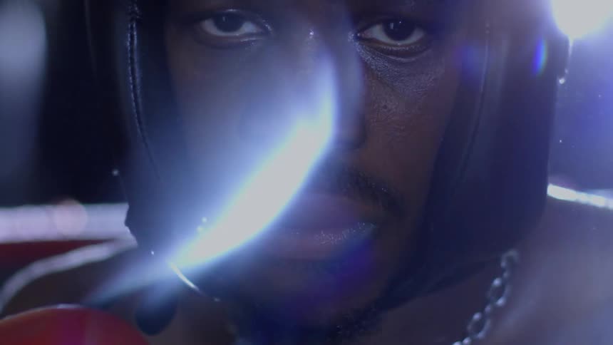 A determined male boxer wearing headgear stares intensely into the camera with dramatic lighting