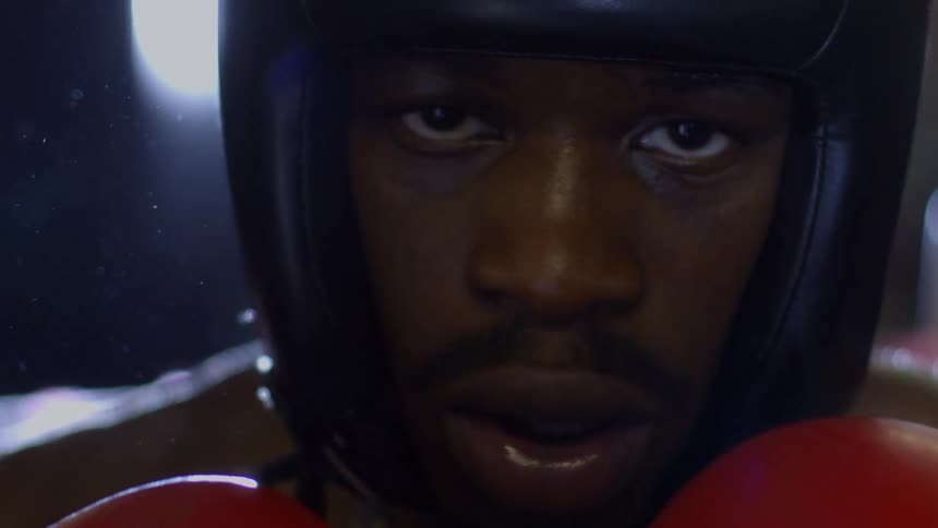 A slow-motion extreme close-up of a focused boxer in headgear with a dramatic lens flare