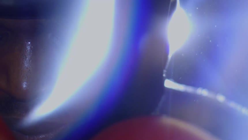 Extreme close-up of a sweaty boxer's face with red gloves up, looking exhausted yet focused in slow motion