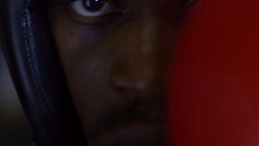 An extreme close-up rack focus reveals the intense eyes of a boxer in headgear with a red glove in front of his face