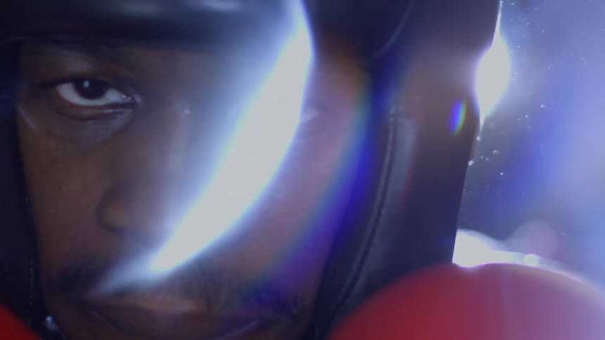 Dramatic close-up of a boxer's face, staring intently at the camera with his red gloves up, ready to fight