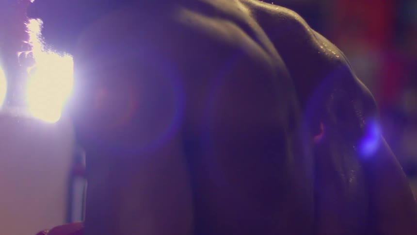A dramatic backlit close-up shows a tired and sweaty boxer resting on the ropes of a boxing ring