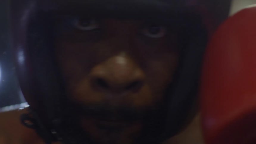 A determined boxer in protective headgear stares intensely forward in a dramatic close-up that ends with a bright lens flare