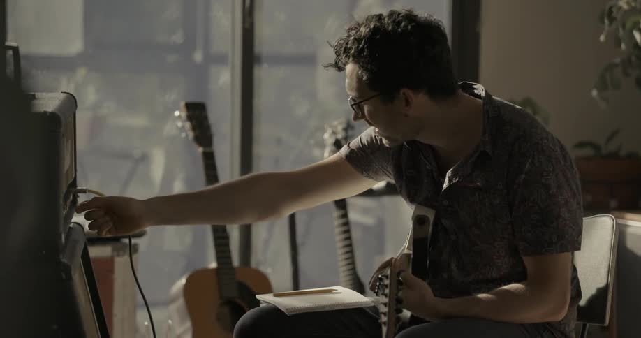 Man adjusting his equipment while playing his guitar