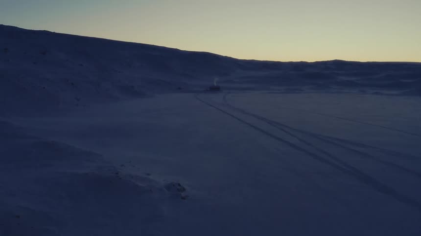 Aerial view of a lonely cabin in a vast, snowy tundra during the blue hour, with smoke curling from its chimney
