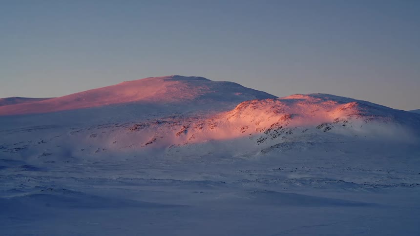 A serene view of pink sunrise light touching the tops of snow-covered arctic hills