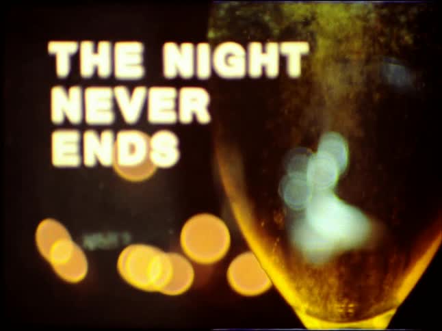 A vintage film title card reading 'The Night Never Ends' is shown next to a bubbling glass of champagne with bokeh lights in the background