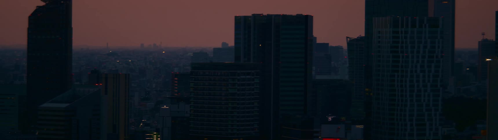 An aerial view of the Tokyo skyline shows the city's towering skyscrapers against a deep purple twilight sky as evening sets in
