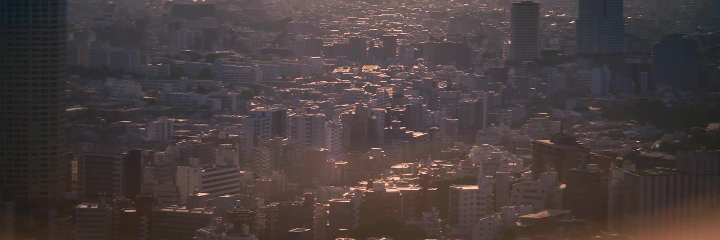 A sprawling cityscape is seen from above, bathed in the warm, hazy light of the golden hour