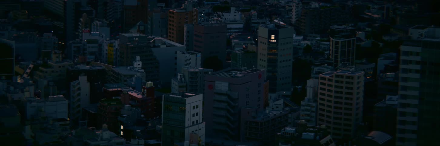 A high-angle static shot captures the dense urban landscape of a Japanese city during the quiet twilight hours