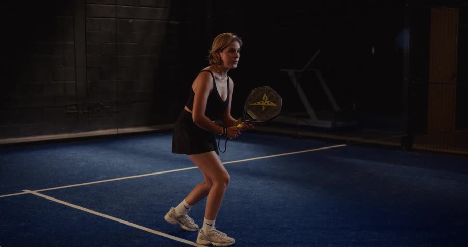 A cinemagraph of a focused woman in athletic wear waiting in a ready stance on a blue indoor padel court