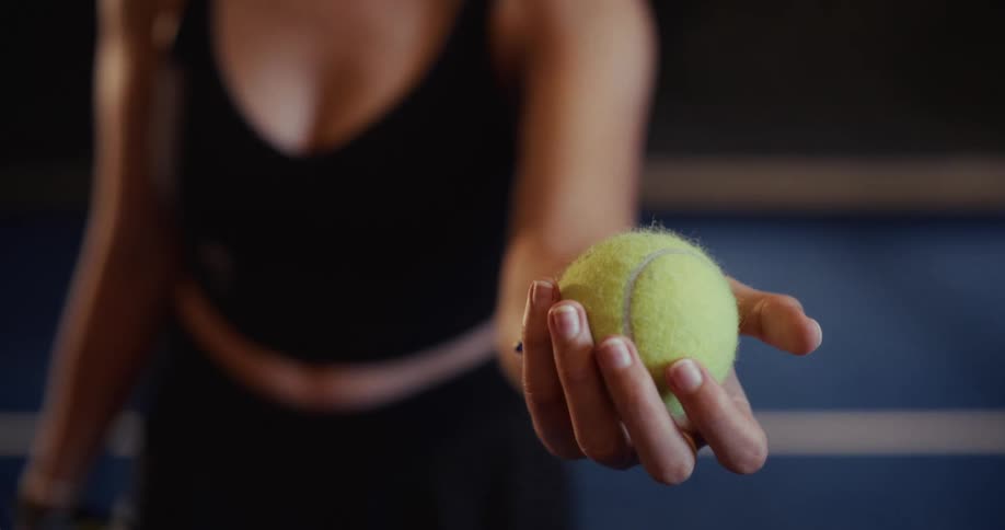 A focused close-up of a woman's hand holding a tennis ball on a court