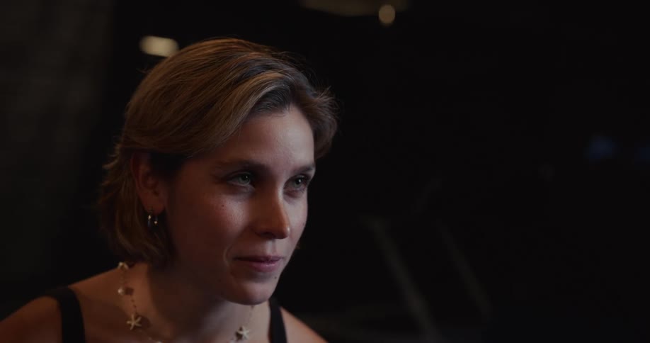 Close-up of a smiling young woman listening intently during a conversation in a dimly lit, intimate setting