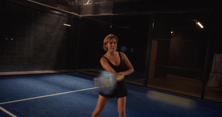 Slow motion shot of a happy woman playing padel tennis, practicing her shots on a blue court