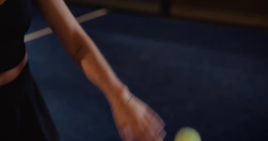 Close-up slow-motion shot of a female tennis player's arm as she tosses and catches a tennis ball on a blue court