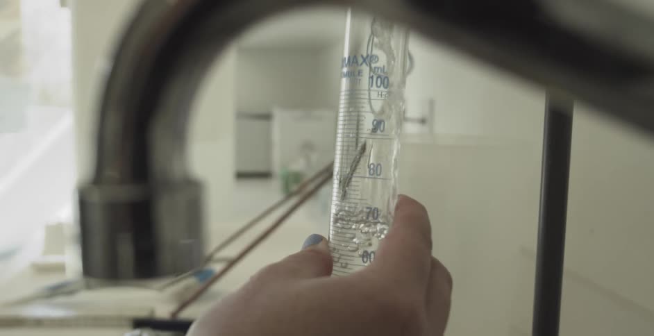Slow-motion close-up of a lab technician carefully filling a graduated cylinder with clear liquid from a tap