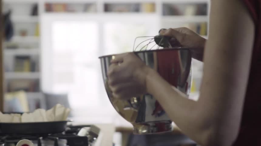 A person moves a mixing bowl over to the stove