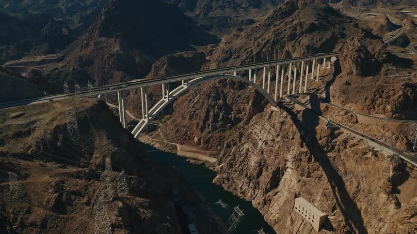 An epic aerial view slowly reveals the Mike O'Callaghan–Pat Tillman Memorial Bridge spanning the Colorado River in a vast desert canyon