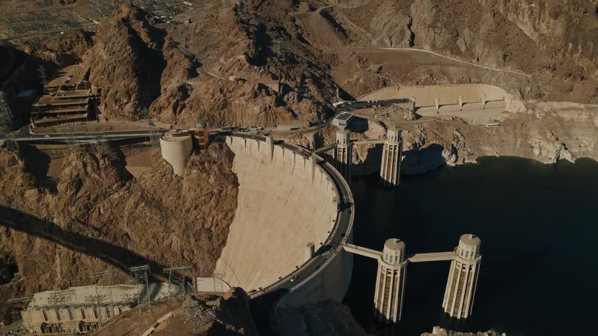 A slow aerial zoom captures the immense scale of the Hoover Dam and the low water levels of Lake Mead on a bright, sunny day