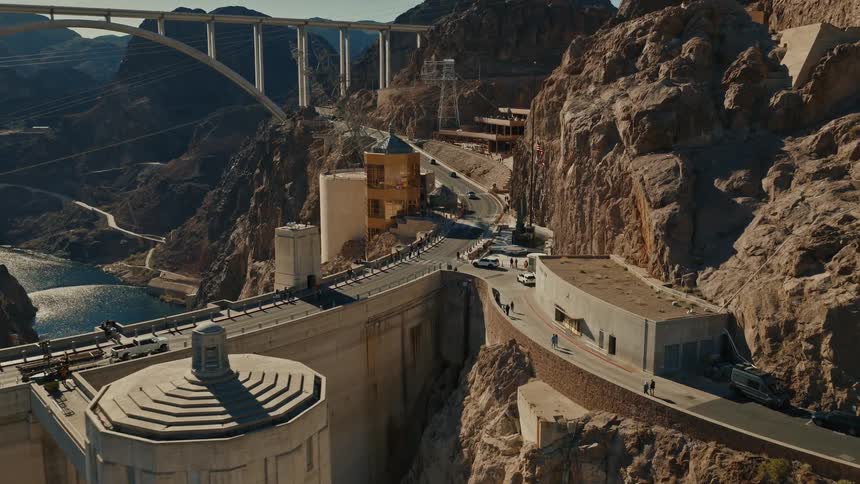 A slow aerial dolly shot reveals the massive Hoover Dam, traffic, and the Mike O'Callaghan–Pat Tillman Memorial Bridge