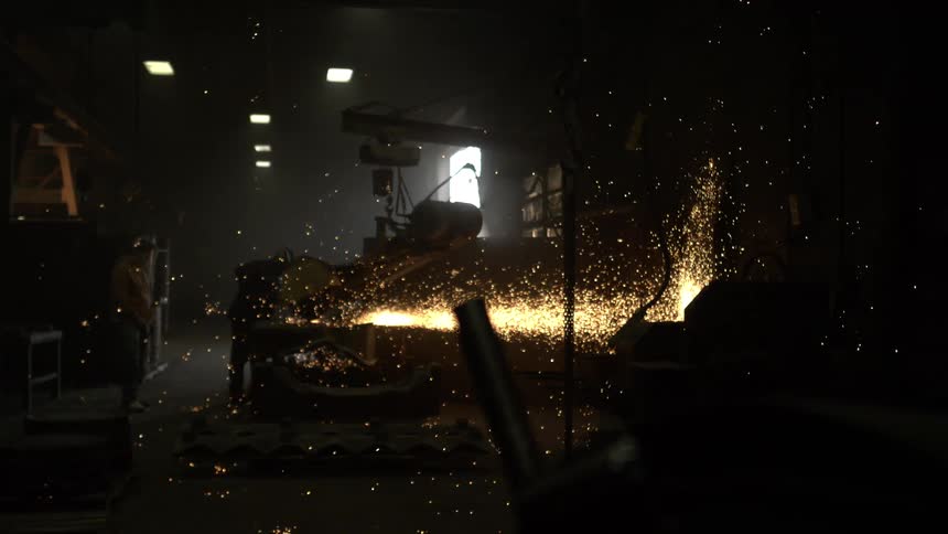 A dramatic slow-motion shot of an industrial saw cutting through metal, sending a brilliant shower of sparks flying in a dark factory